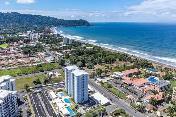 Aerial view of beachfront resort town with high-rise hotels, sandy beach, turquoise ocean, and forested headland